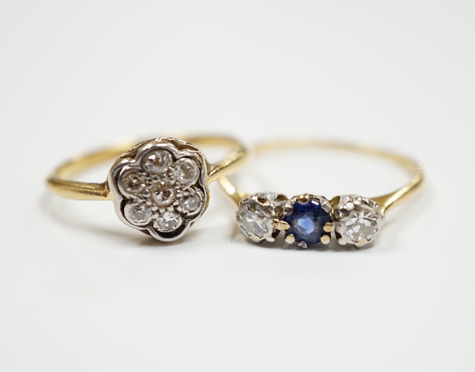A 1920's 18ct, plat and diamond cluster set flower head ring, size M/N and a 18ct and plat. sapphire and diamond set three stone ring, size O/P, gross 3.9 grams.